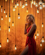 A beautiful blonde woman in a long red dress is looking at the LED Edison lamps in a retro style that lights brightly with warm light.