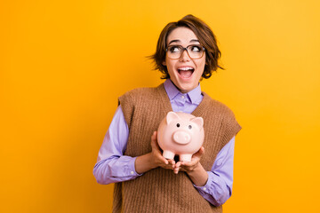 Sticker - Photo of impressed girl dressed knitwear waistcoat in glasses hold piggy box look at sale empty space isolated on yellow color background