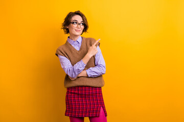 Wall Mural - Portrait of optimistic woman wear knit waistcoat in glasses directing look at offer empty space isolated on yellow color background