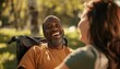 © LoLArt - Happy black disabled african american middle aged man laughing in wheel chair and a female woman caregiver nurse taking care of him outdoors in a park on sunny day