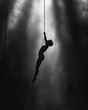 Solitary silhouette of a person hanging from a trapeze in a dimly lit circus tent. The image conveys a sense of suspense and tension, highlighting the human form against a stark background.