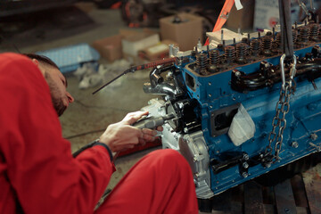 Closeup shot of a mechanic in a red uniform mounting the car engine