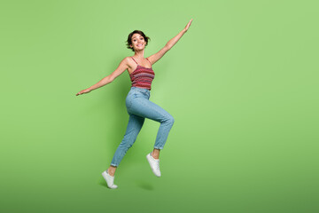 Wall Mural - Full length photo of carefree positive cute girl wear stylish outfit flying air going empty space isolated on green color background