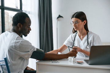 Sitting by a table. Female doctor measures blood pressure of a man