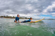 Happy boy learns to surf - young surfer learn to ride on surfboard with surf instructor on sea waves. Active family lifestyle, kids outdoor water sport lessons.