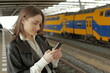 Portrait of a young woman using mobile phone waiting for a train at a station 