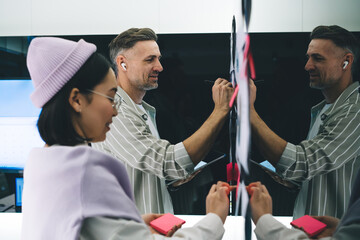 Fototapete - Caucasian male in bluetooth earbuds collaborate with female colleague during brainstorming in office interior, professional employees analyzing business strategy and startup project in board room