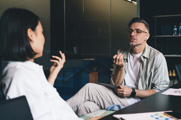 Fototapete - Serious Caucasian man in optical spectacles for vision protection holding modern touch pad and have argue with colleague, male employee in eyeglasses and earbuds discussing business ideas with partner