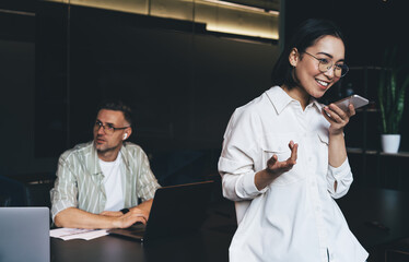 Fototapete - Happy Asian woman in eyewear for vision protection using mobile application for record audio notes during working day in office, successful female employee in spectacles communicate via cellphone