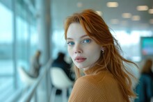 A Woman With Red Hair And Blue Eyes Is Sitting In A Cafe. She Is Wearing A Brown Sweater And Has Her Hair Blowing In The Wind