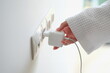 Woman hand in robe gown inserts white charger into socket in hotel rooms or at home. Charge gadgets correctly concept