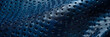 A detailed shot of electric blue leather with perforated holes creating a textured pattern. The leather has a glossy finish resembling metal, with a hint of darkness and moisture