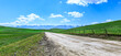 Rural dirt road and green meadow with mountain nature landscape in summer. Panoramic view.