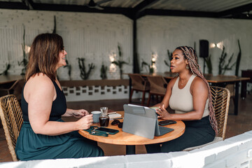 stylish café, two professional women immersed in business meeting. woman with long braids discusses 