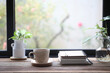 Coffee in a white cup and notebooks on wooden table with plants