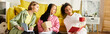 © LIGHTFIELD STUDIOS - Diverse group of young women laughing and studying on top of a bright yellow couch in a cozy home setting.
