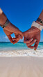 dwoje ludzi na plaży trzyma się za ręce, w oddali morze, słońce, fale