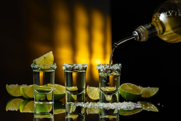 Wall Mural - Gold tequila with sea salt and lime slices on a black reflective background.