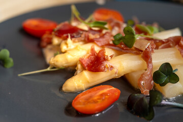 Wall Mural - A plate of Ham and white asparagus on a blue plate. The dish is topped with a garnish of green leaves. Spanish Food