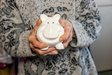 Fototapeta  - Elderly woman holds a piggy bank in her hands, concept of saving money for retirement