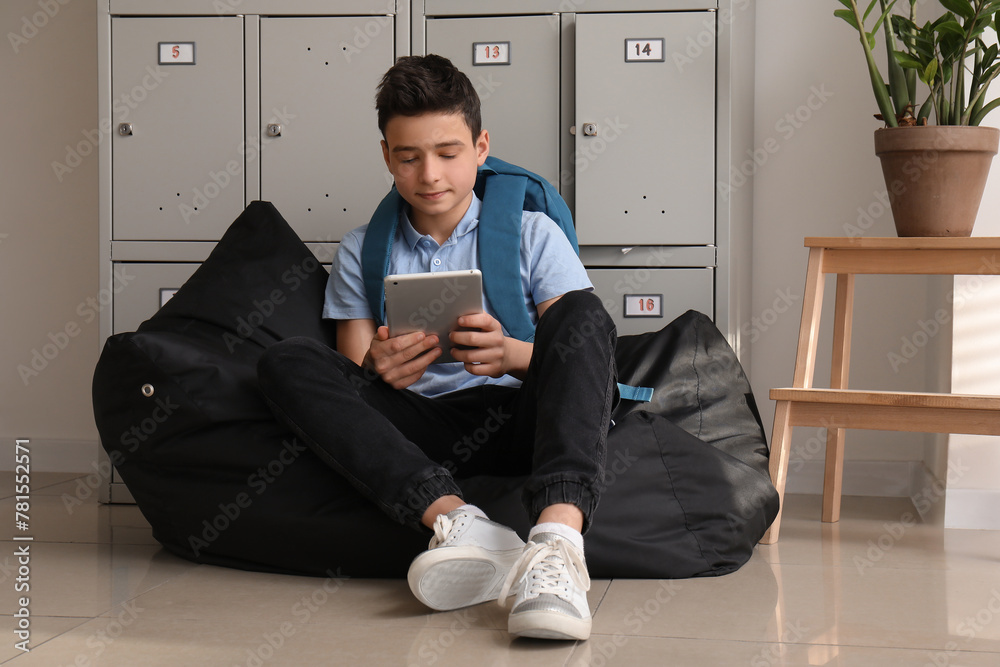 Little boy using tablet computer near locker at school