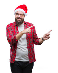 Sticker - Young caucasian man wearing christmas hat over isolated background smiling and looking at the camera pointing with two hands and fingers to the side.