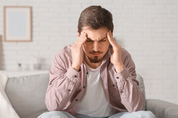 Canvas Print - Tired young man with headache sitting on sofa at home