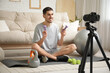 © Pixel-Shot - Sporty happy male blogger with dumbbells and kettlebell recording video at home