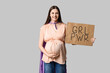 Beautiful young pregnant woman in superhero cape holding cardboard with text GRL PWR on grey background