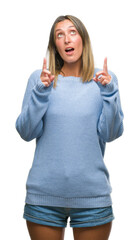 Poster - Young beautiful woman wearing winter sweater over isolated background amazed and surprised looking up and pointing with fingers and raised arms.