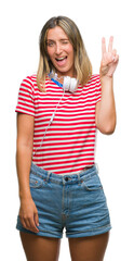 Poster - Young beautiful woman listening music wearing headphones over isolated background smiling with happy face winking at the camera doing victory sign. Number two.