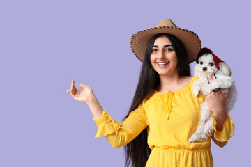 Wall Mural - Young happy woman in hat holding her Bolognese dog on lilac background