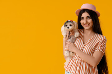 Wall Mural - Young happy woman in hat holding her cute Bolognese dog on yellow background