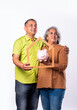 Indian mid age senior couple standing against while background with piggy bank, 3d house model real estate concept
