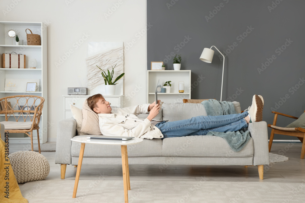 Young man using modern tablet computer on sofa at home