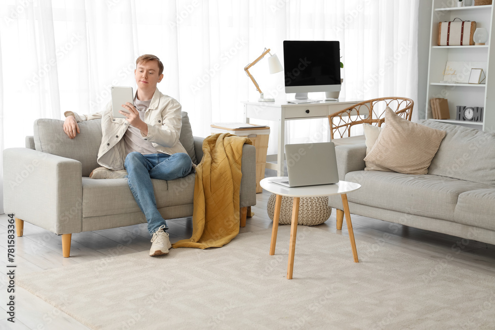 Young man using modern tablet computer on sofa at home