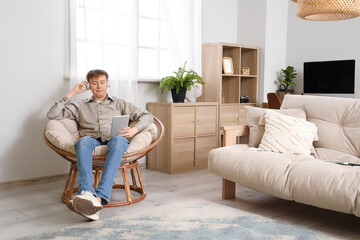 Young man with headphones using tablet computer in armchair at home