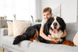 Little boy hugging Bernese mountain dog on sofa at home