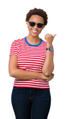 Sticker - Beautiful young african american woman wearing sunglasses over isolated background smiling with happy face looking and pointing to the side with thumb up.