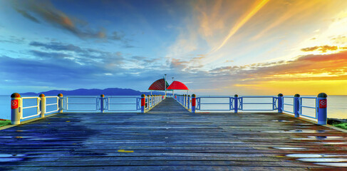 Wall Mural - a pier that is connected to the ocean at sunset with a umbrella