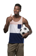 Canvas Print - Young african american man holding soccer football ball surprised with an idea or question pointing finger with happy face, number one