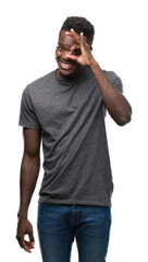 Poster - Young african american man wearing grey t-shirt doing ok gesture with hand smiling, eye looking through fingers with happy face.