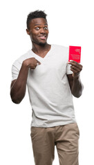 Sticker - Young african american man holding passport of Switzerland with surprise face pointing finger to himself