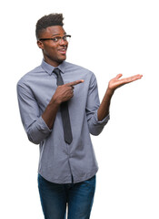 Canvas Print - Young african american business man over isolated background amazed and smiling to the camera while presenting with hand and pointing with finger.