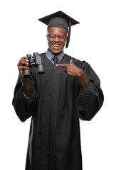 Sticker - Young graduated african american man looking for a job using binoculars very happy pointing with hand and finger