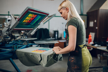 Wall Mural - Print shop worker taking screen printed t-shirt of machine at facility