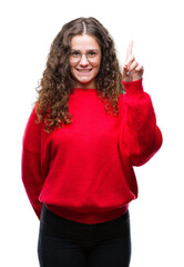 Wall Mural - Beautiful brunette curly hair young girl wearing glasses and winter sweater over isolated background showing and pointing up with finger number one while smiling confident and happy.