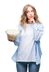 Poster - Beautiful young blonde woman eating popcorn over isolated background serious face thinking about question, very confused idea