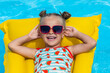 Cute little girl lying on inflatable mattress in swimming pool with blue water on warm day on tropical vacations. Summertime activities concept. advertising of tour operators and all-inclusive hotels