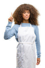 Canvas Print - African american shop owner woman wearing an apron raising finger, the number one